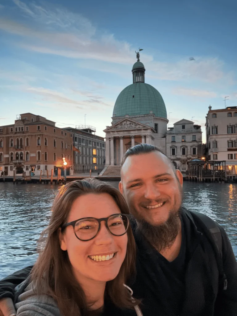 a man and woman taking a selfie in front of water with buildings and a dome